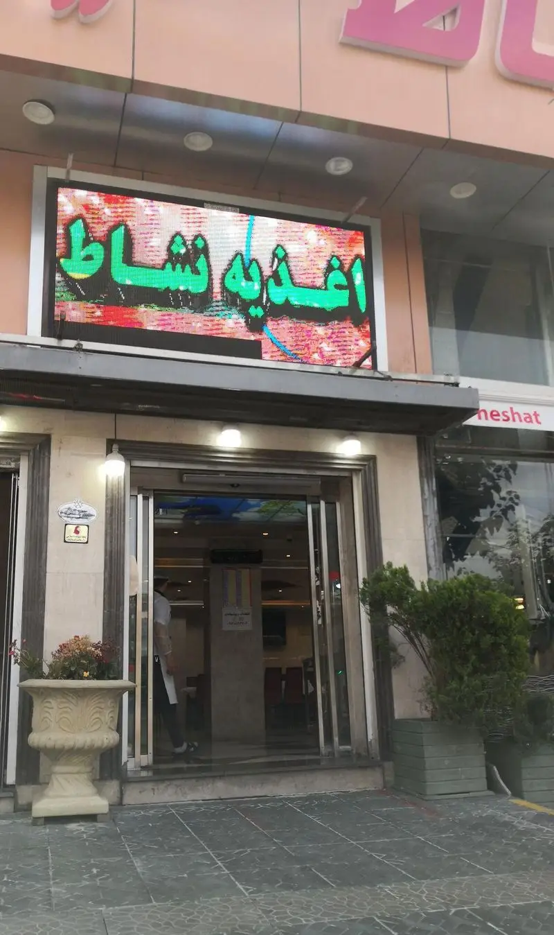 تصویری از نمای ورودی اغذیه نشاط، یک کسب و کار غذا با تابلوی LED دیجیتال و روشن، محیطی دلنشین برای مشتریان در حال ورود.