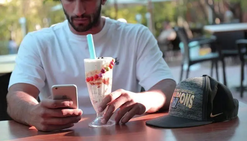 مردی در حال استراحت در کافه باشگاه مینی گلف، با گوشی خود و دسری خنک روی میز. لحظاتی دلپذیر پس از یک بازی هیجان‌انگیز مینی گلف.