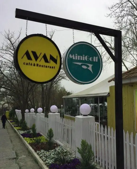 تابلوی ورودی باشگاه مینی گلف و کافه رستوران آوان، با تابلوهای جذاب و فضای سبز دلنشین. حصار سفید و گل‌های رنگی جلوه‌ای زیبا داده‌اند.