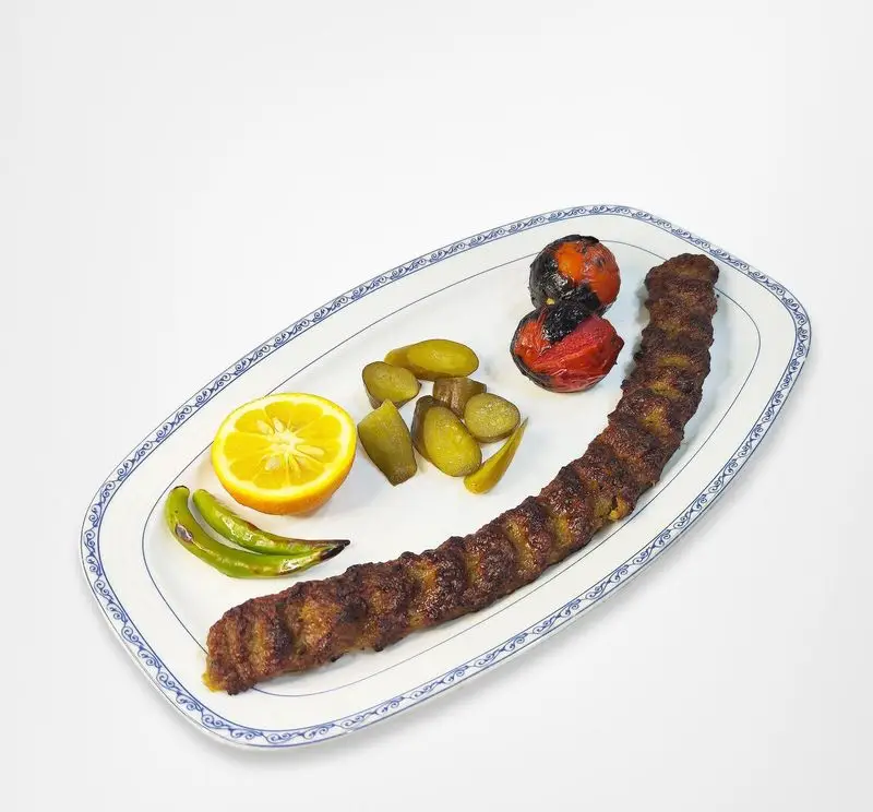 کباب کوبیده رستوران امینی سرو شده در بشقاب با گوجه کبابی، فلفل، لیمو و خیارشور؛ غذای اصیل و دلنشین ایرانی.