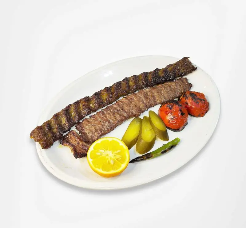 کباب کوبیده ممتاز رستوران امینی، سرو شده با گوجه و فلفل کبابی، لیمو تازه و خیارشور، تجربه‌ای اصیل از غذای ناب ایرانی.