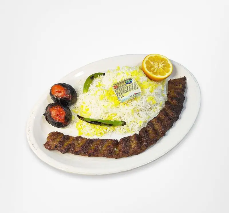 چلوکباب کوبیده لذیذ رستوران امینی شامل برنج، کباب گوشت، گوجه کبابی، لیمو و کره.