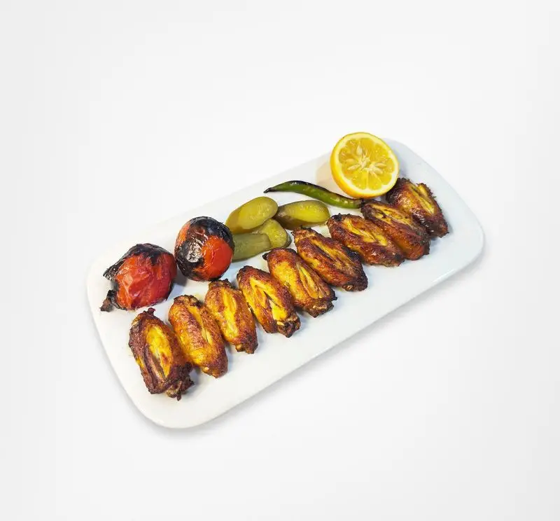 بال و بازوی کبابی طلایی و لذیذ رستوران امینی، سرو شده با گوجه کبابی، خیارشور، لیمو و فلفل سبز تازه.