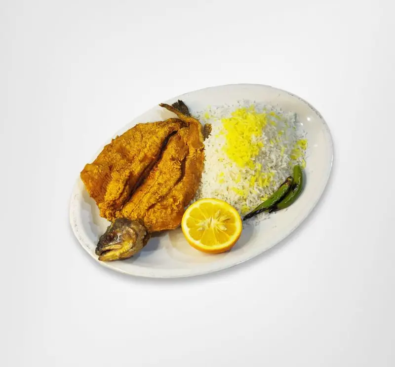 تصویری از یک پرس ماهی سرخ شده طلایی و خوشمزه همراه با برنج زعفرانی، برش نارنج تازه و فلفل سبز در رستوران امینی.
