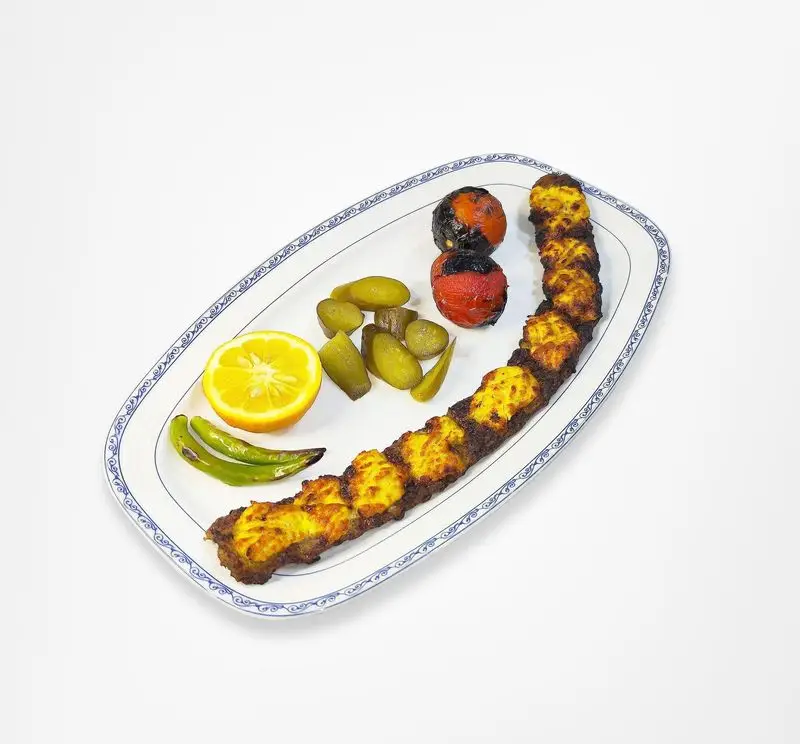 دیس کباب رستوران امینی با گوجه کبابی، فلفل سبز، لیمو تازه و خیارشور، غذایی سنتی و خوشمزه برای لذت بردن از طعم اصیل ایرانی.