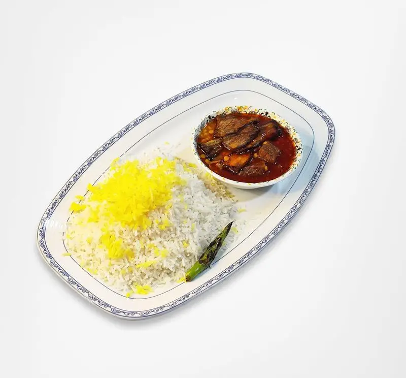 یک پرس غذای ایرانی شامل خورش بادمجان لذیذ با تکه‌های گوشت و لپه، همراه با پلو زعفرانی و فلفل، سرو شده در رستوران امینی.
