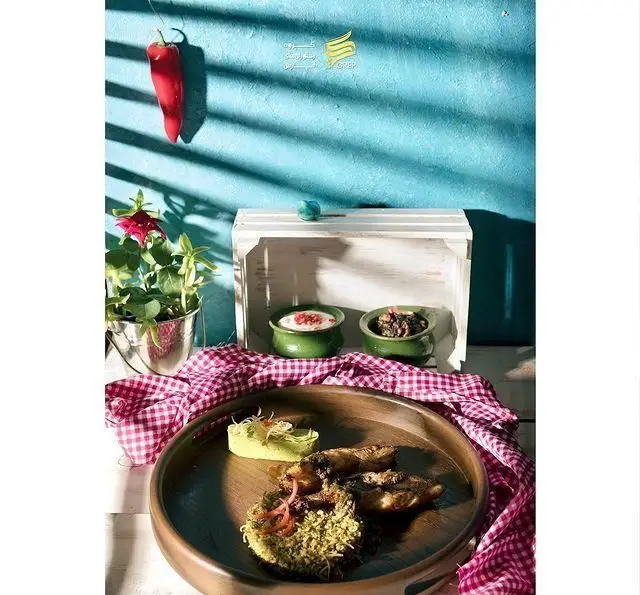چیدمان جذاب غذای ایرانی کافه رستوران گرپ: ماهی با پلوهای خوش‌عطر، ماست و خورشت، روی میز با دیوار آبی و فلفل قرمز.
