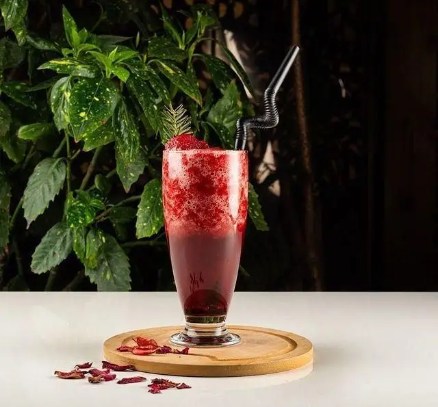 کوکتل یا اسموتی توت فرنگی خنک و خوشمزه کافه رستوران گرپ روی میز چوبی با گلبرگ، انتخابی دلپذیر در فضای سرسبز.