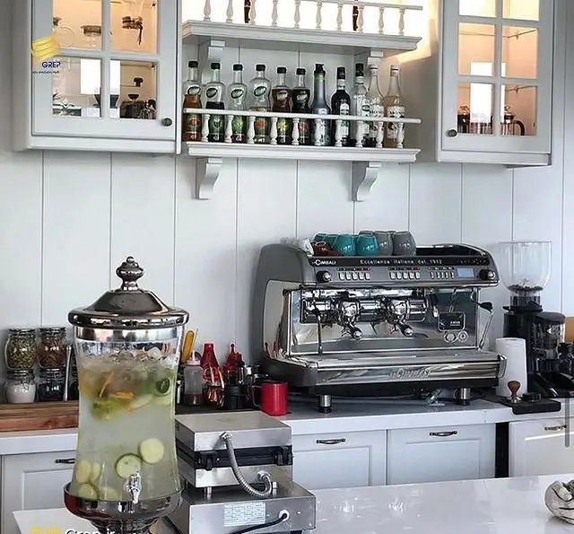 تجهیزات کامل کافه رستوران گرپ: دستگاه اسپرسو حرفه ای، سیروپ های متنوع و نوشیدنی خنک در فضای روشن و شیک کافه.