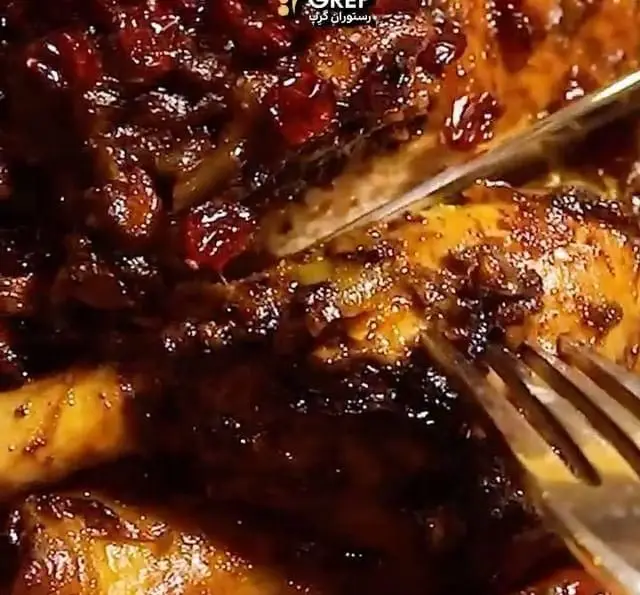 نمای نزدیک از مرغ خوش پخت و مجلسی با سس ملس و زرشک در کافه رستوران گرپ، در حال آماده شدن برای سرو با چاقو و چنگال.