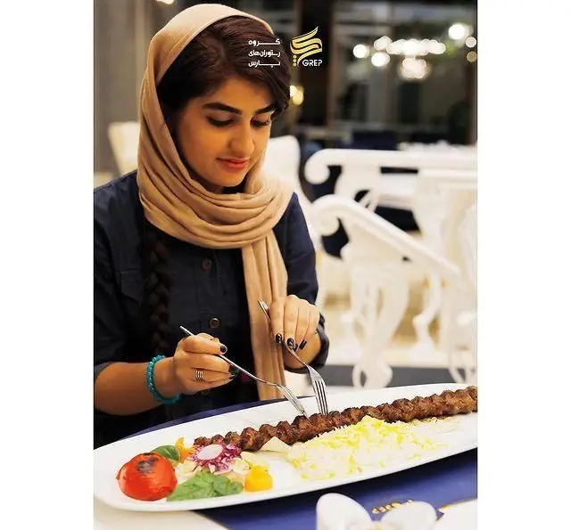 خانمی با حجاب زیبا در کافه رستوران گرپ، از سرو کباب کوبیده و چلو زعفرانی لذت می‌برد. تجربه غذایی بی‌نظیر.