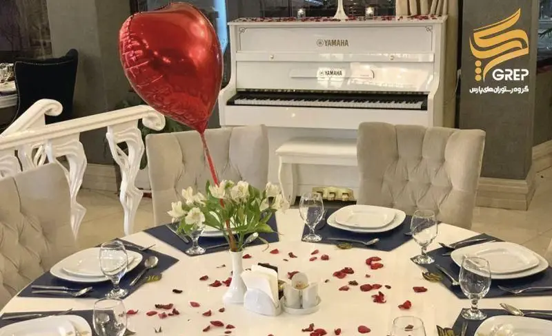 میز شام رمانتیک در کافه رستوران گرپ، با دکوراسیون لوکس، گل، گلبرگ و بادکنک قلب، در کنار پیانو Yamaha. فضایی دلنشین از گرپ پارس.