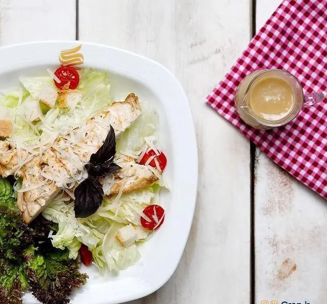 نمایی از سالاد سزار مرغ کلاسیک و دلپذیر کافه رستوران گرپ، همراه با کاهو تازه، تکه‌های مرغ گریل، پنیر پارمزان و سس مخصوص.