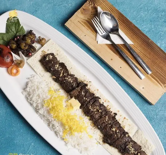 تصویری زیبا از چلوکباب لذیذ و اصیل ایرانی در کافه رستوران گرپ، با برنج زعفرانی، کره، گوجه و سبزیجات.