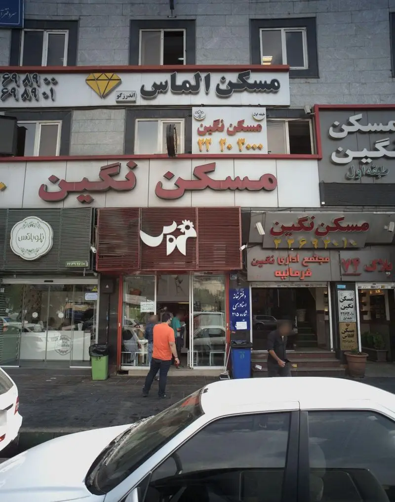 نمای بیرونی شلوغ فست فود خروس، رستوران محبوب در خیابان‌های تهران، در کنار آژانس‌های املاک مسکن الماس و نگین.