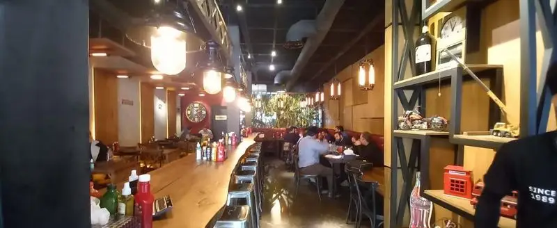 نمایی از فضای داخلی رستوران میخوش، با دکوراسیون مدرن و صنعتی، مشتریان در حال صرف غذا، میزهای شیک و بار بلند چوبی. محیطی دلنشین برای کافه و غذاخوری.