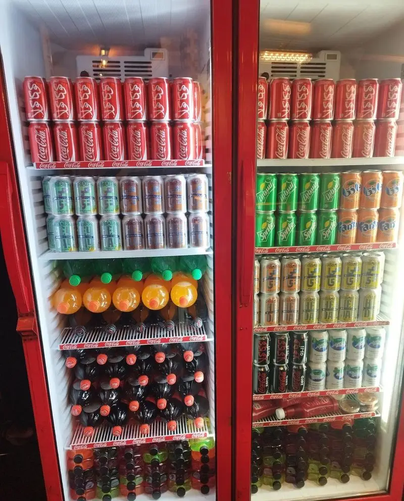 دو یخچال بزرگ قرمز رنگ پر از قوطی‌های کوکاکولا، اسپرایت، فانتا و انواع آبمیوه و نوشیدنی‌های خنک در رستوران میخوش.