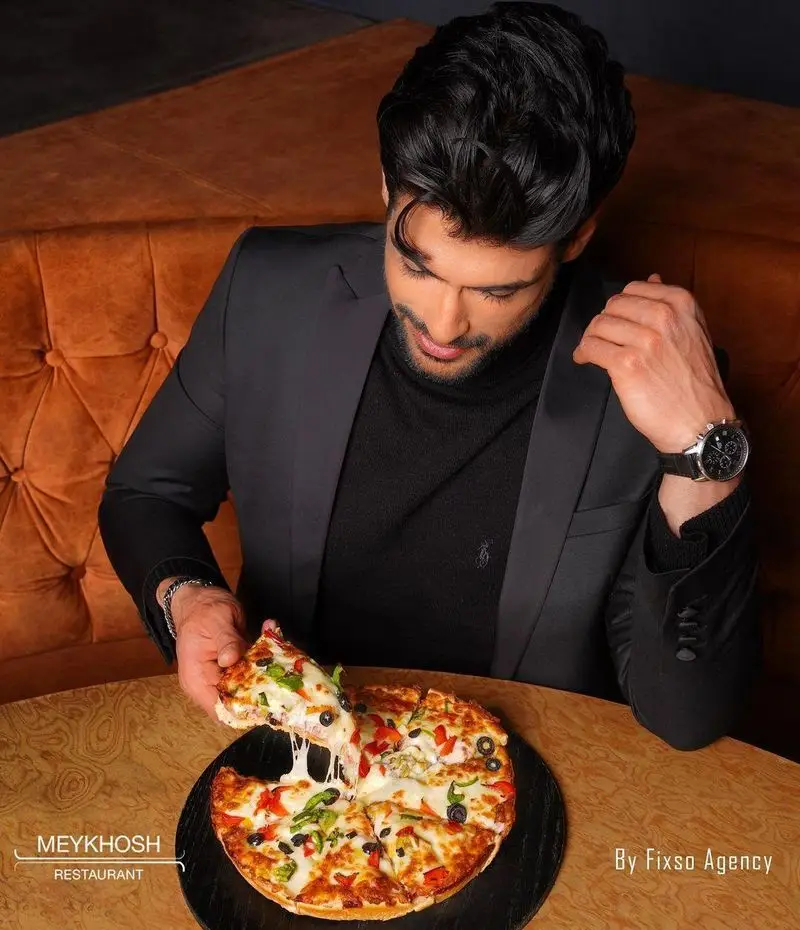در رستوران میخوش، مردی خوش‌پوش و شیک در حال لذت بردن از پیتزای تازه و داغ با پنیر کشسان، زیتون و فلفل است.