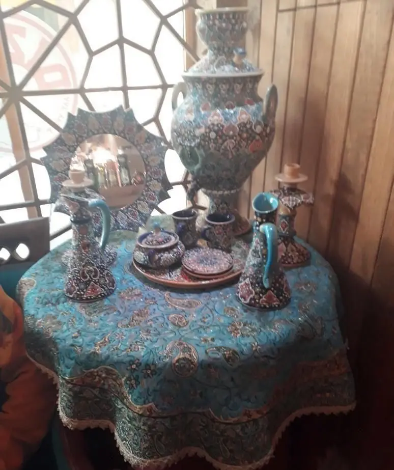 ظروف سنتی میناکاری شامل سماور، آینه و پارچ در کافی شاپ دیزی تو، دکوری زیبا برای تجربه چای ایرانی و محیط دلنشین.