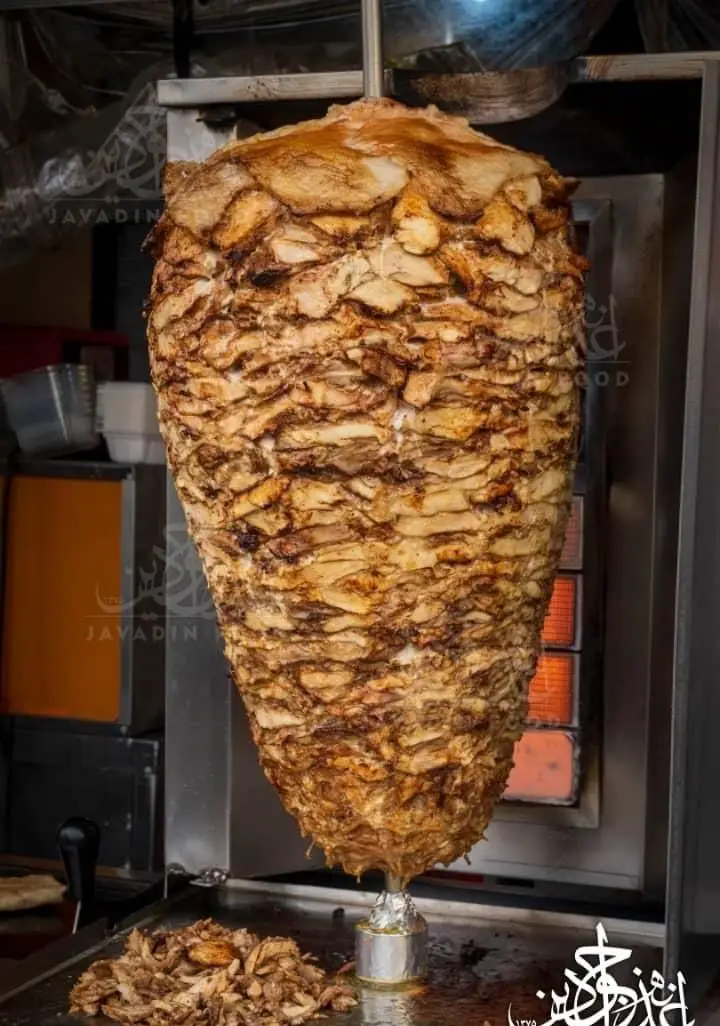 شاورما مرغ بزرگ و آبدار اغذیه جوادین با گوشت تازه و طلایی، در حال آماده‌سازی برای ساندویچ‌های خوشمزه و داغ.