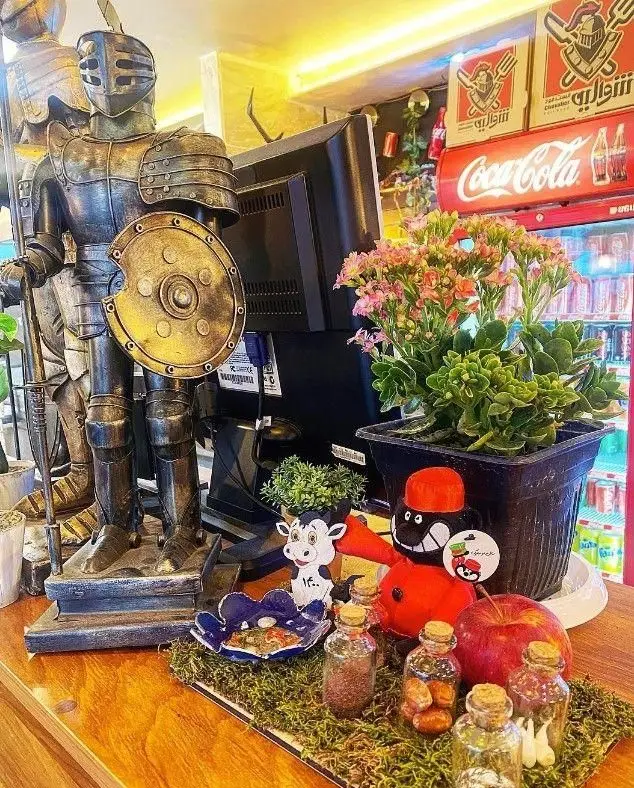 پیشخوان فست فود شوالیه با مجسمه شوالیه، گیاهان، مانیتور و یخچال کوکاکولا، منعکس‌کننده محیط منحصربه‌فرد.