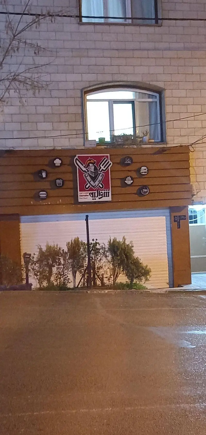 نمای بیرونی فست فود شوالیه با تابلوی اصلی شامل طرح شوالیه، شمشیر و چنگال و آیکون‌های همبرگر و سیب زمینی.