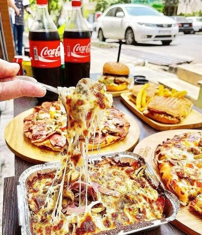 انواع پیتزا، برگر و ساندویچ‌های خوشمزه در فست فود شوالیه با پنیر کشی عالی. نوشابه کوکاکولا در کنار غذای آماده.