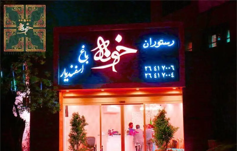 نمای شب رستوران بین المللی خوارزمی با تابلو نئون روشن شامل نام رستوران و اطلاعات تماس. ورودی شیشه‌ای و نمای کلی ساختمان.