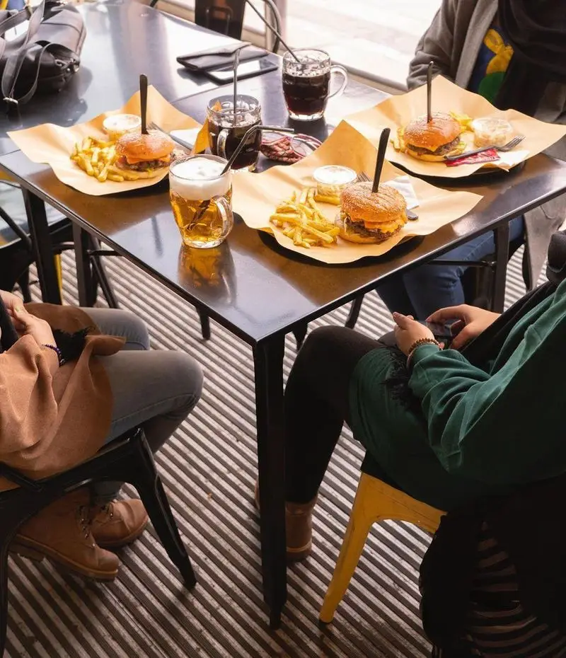 وعده غذایی لذیذ در کیوسک برگر: سه برگر آبدار با سیب‌زمینی‌های طلایی و نوشیدنی‌های خنک روی میز، تجربه‌ای دلنشین برای مشتریان.