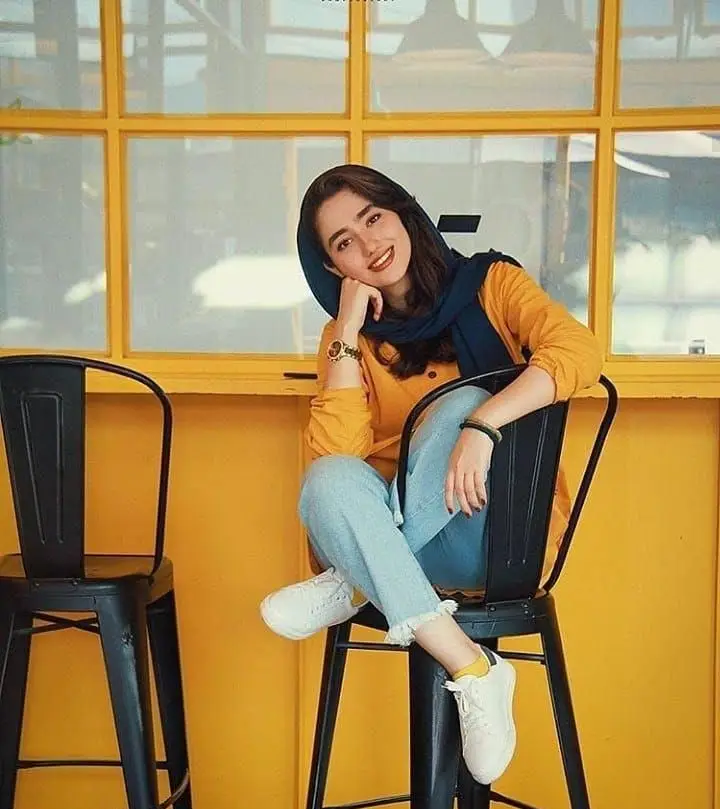 دختر جوان شاد با حجاب در محیط دلنشین کیوسک برگر با دکوراسیون زرد و صندلی مدرن. تجربه مشتری مثبت در فضای رستوران.