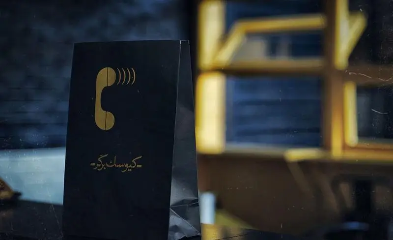کیسه مشکی برند "کیوسک برگر" با نشان تلفن طلایی و امواج صوتی، نشان‌دهنده خدمات سفارش آنلاین و تحویل غذا.