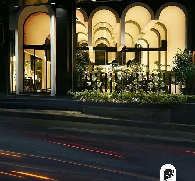 نمای بیرونی فست فود و کافی شاپ لمنز در شب، با معماری قوسی مدرن، نورپردازی دلپذیر و فضای سبز زیبا در کنار خیابان.