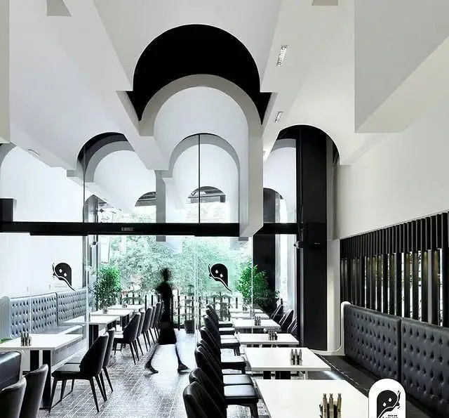 فضای داخلی زیبا و مدرن فست فود و کافی شاپ لمنز با تم سفید و مشکی، سقف طاق‌دار، مبلمان راحت و چشم‌انداز دلنشین فضای سبز.