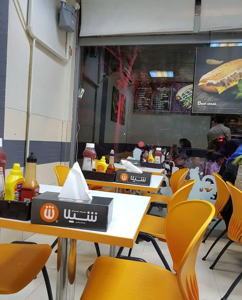 تصویری از فضای داخلی فست فود زنجیره‌ای شیلا با دکوراسیون گرم، میز و صندلی‌های زرد و محیطی دلنشین برای صرف انواع غذا.