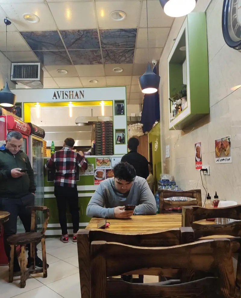 محیط داخلی فست فود پیتزا آویشن با مشتریان در حال انتظار و سفارش غذا، مکانی دلنشین برای صرف یک وعده سریع و خوشمزه.