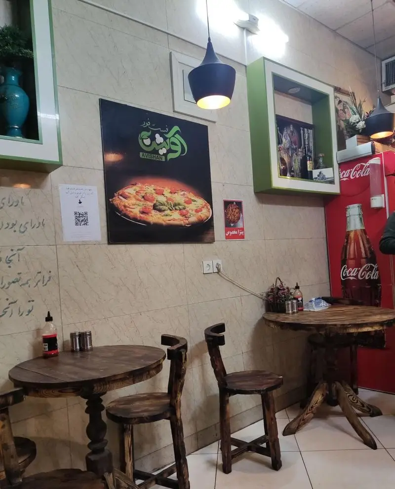 دکوراسیون داخلی فست فود پیتزا آویشن با میز و صندلی‌های چوبی دست‌ساز و فضای دنج. پوستری از پیتزا و محیطی گرم و دلنشین برای مشتریان.