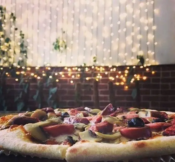 پیتزای خوشمزه با قارچ، سوسیس و زیتون در رستوران پروفسور. تصویری دلنشین از محیط با نورپردازی گرم و جذاب. ایده‌آل برای شام یا ناهار.