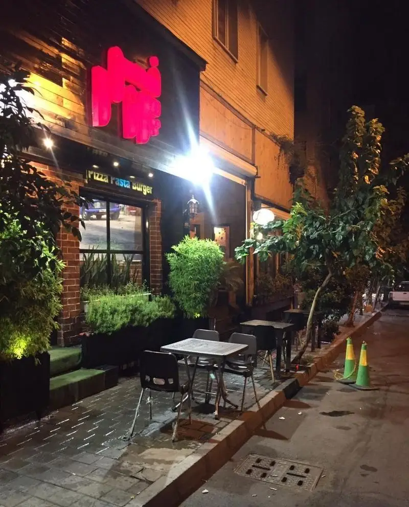 رستوران پروفسور در شب با تابلوی نئون قرمز روشن. نمای بیرونی با فضای باز، میز و صندلی برای سرو پیتزا، پاستا و برگر.