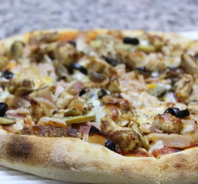 پیتزا مخصوص رستوران پروفسور با تکه‌های مرغ گریل شده، زیتون سیاه و پنیر فراوان، آماده سرو در محیطی دلنشین.