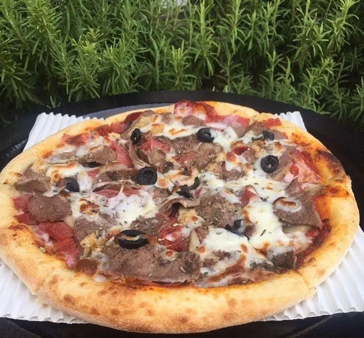 پیتزا مخصوص گوشت و زیتون رستوران پروفسور، با پنیر فراوان و خمیر پیتزای عالی، آماده سرو در فضایی دلنشین و سرسبز.