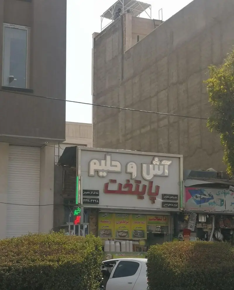 رستوران سنتی آش و حلیم پایتخت با تابلو بزرگ، منوی متنوع غذاهای ایرانی شامل آش، حلیم، عدسی، باقالی پلو و شماره تماس برای سفارشات.