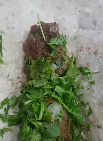 کباب لقمه مخصوص رضا لقمه، پیچیده در نان تازه، با مقدار فراوان سبزیجات معطر (جعفری) و پاشیدن سماق، یک غذای سنتی و محبوب ایرانی.