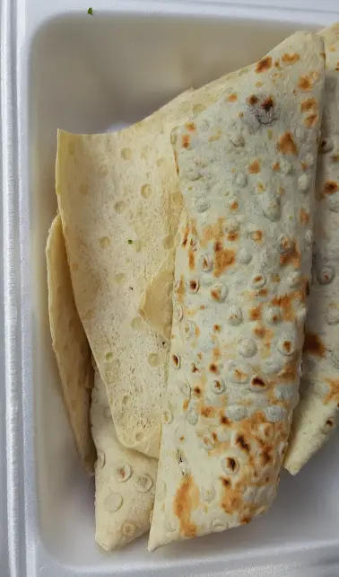 لقمه‌های خوش‌طعم و تازه رضا لقمه، چند رول ساندویچی نان با بافت خاص و نقاط برشته در ظرف سفید بیرون‌بر. غذایی لذیذ.