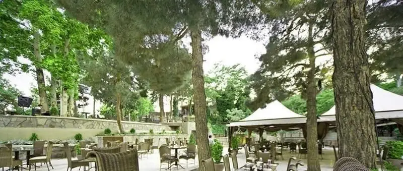 نمایی دلنشین از رستوران آبشار گیله وا، شامل فضای باز با چیدمان میز و صندلی در طبیعت سرسبز و زیر سایه درختان و سایه‌بان‌های شیک