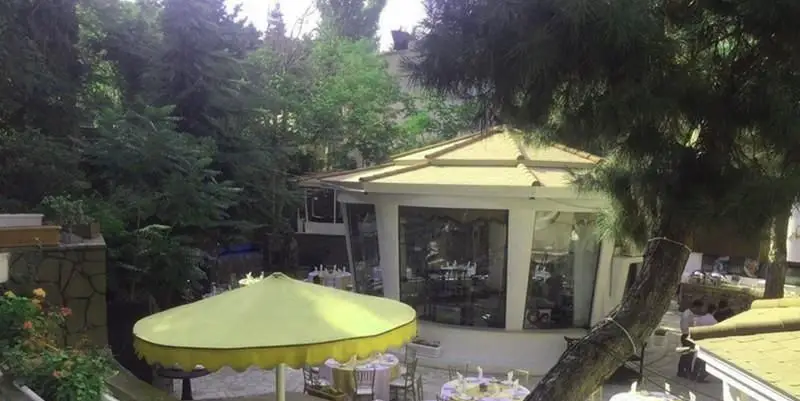 فضای سرسبز و دلنشین آبشار گیله وا، باغ رستورانی با آلاچیق، میز و صندلی برای پذیرایی در طبیعت و محیطی آرامش‌بخش.