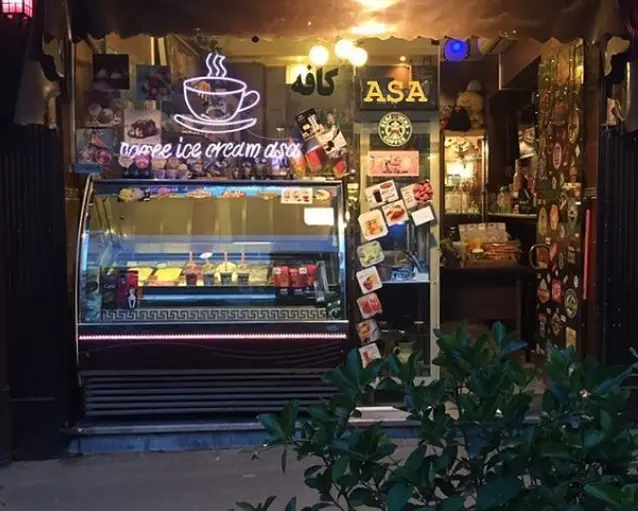 نمای شبانه کافه آسا با تابلوی نئون قهوه، ویترین بستنی و دسرهای متنوع، لوگوی ASA و کافه، و ورودی دنج و روشن.