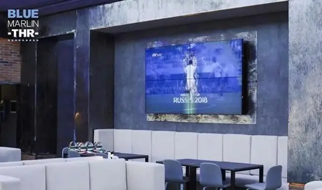 تصویری از فضای داخلی کافی شاپ بلومارلین تهران با دکوراسیون مدرن و مبلمان سفید، مجهز به تلویزیون بزرگ برای تماشای فوتبال