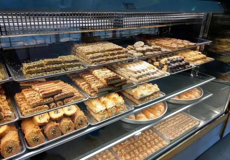 ویترین پر از انواع شیرینی‌های سنتی و تازه قنادی آرامیس، شامل باقلوا، کلوچه و دسرهای لذیذ با مغز پسته و گردو. انتخابی عالی.