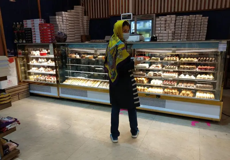 تصویری از قنادی و شیرینی آرامیس: مشتری در حال خرید از ویترین زیبای پر از انواع کیک، شیرینی و دسرهای خوشمزه.