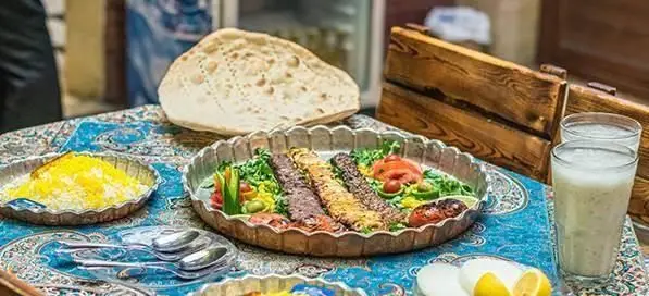 کباب ایرانی با برنج زعفرانی، نان تازه و دوغ در سفره خانه سنتی باغچه. لذت غذای اصیل و فضای دلنشین ایرانی.